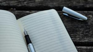 Blank lined notebook page with an uncapped fountain pen resting on it.