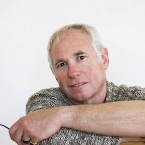 White male with gray hair wearing green sweater and holding glasses